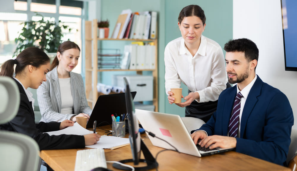 Young woman bringing coffee to male colleague in office