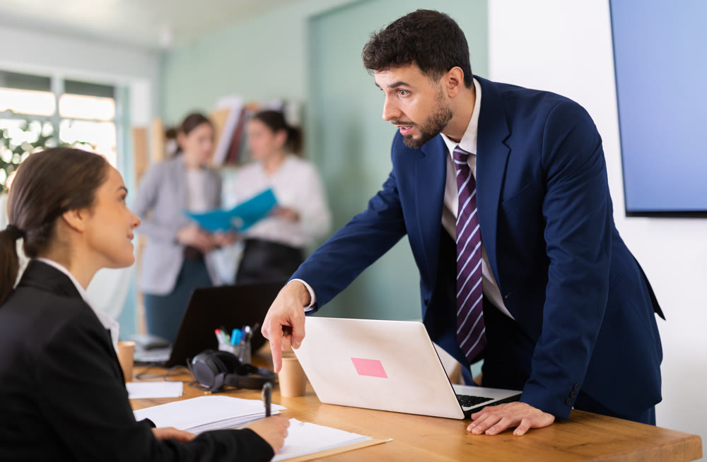 Male manager leaning over table and instructing young employee