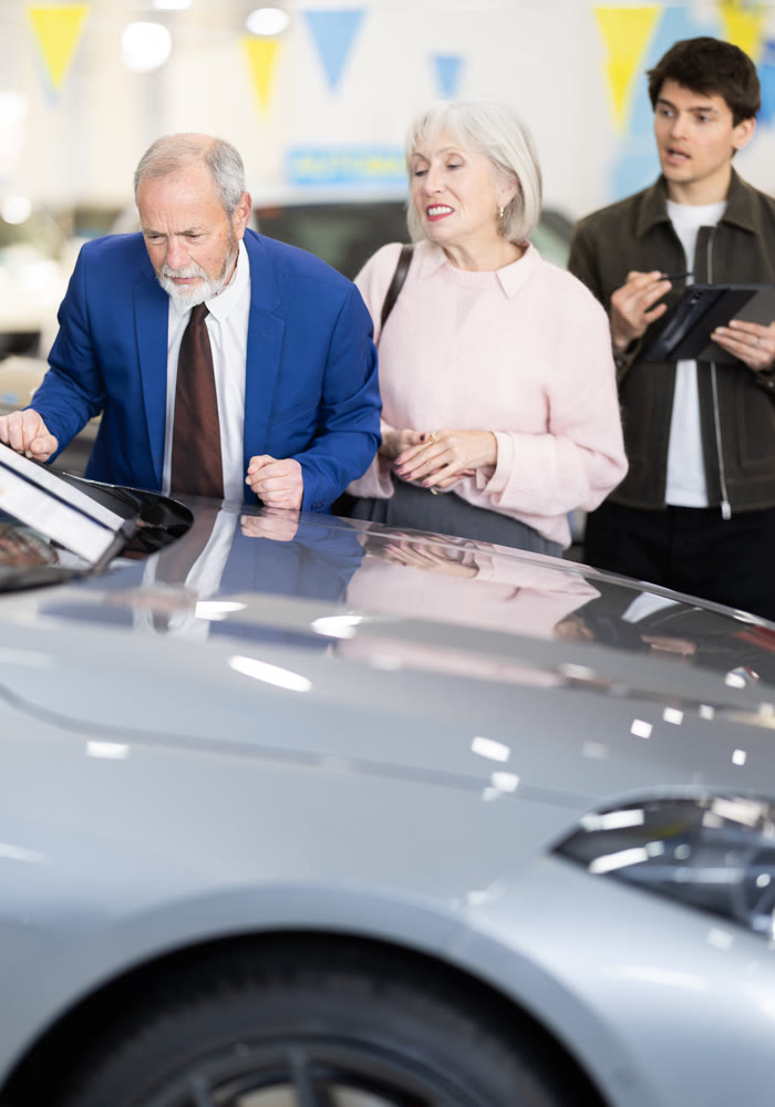 Yung male salesman sells car to mature couple at car dealership