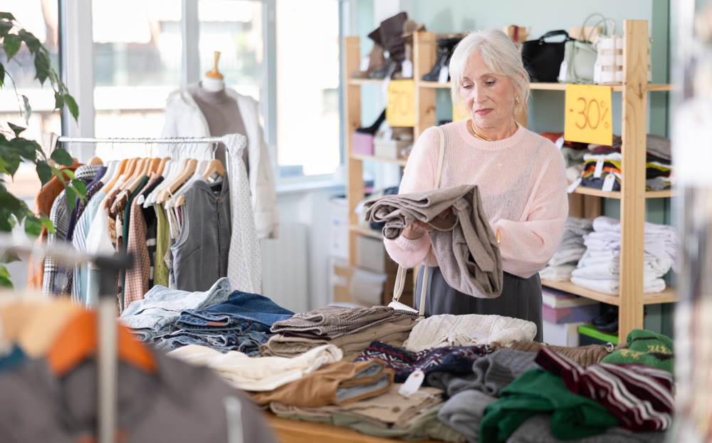 Focused happy elderly woman client choosing pants or stylish trousers in clothing mall