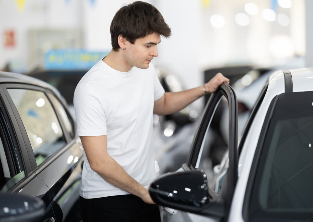 Guy checking, examining new car before making purchase in dealership. man look at auto and touch it