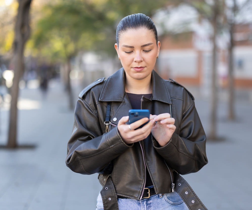 Young woman with phone walking along city street