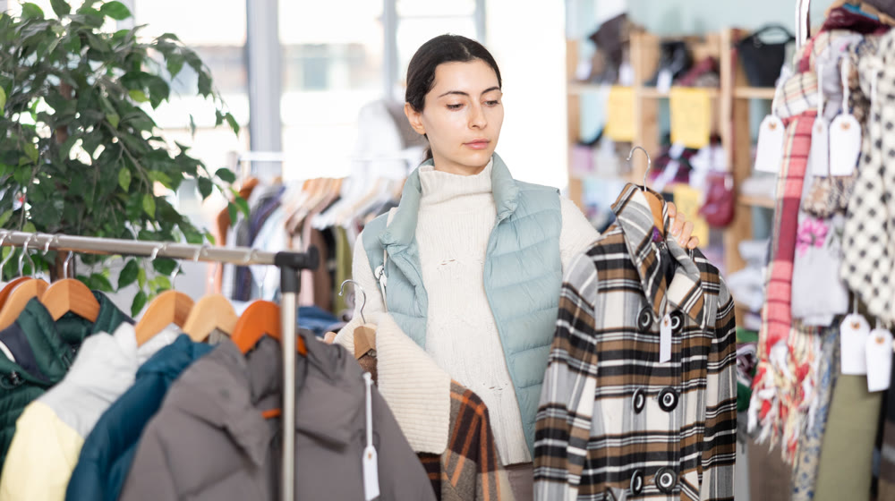 Young woman chooses coat in clothing store