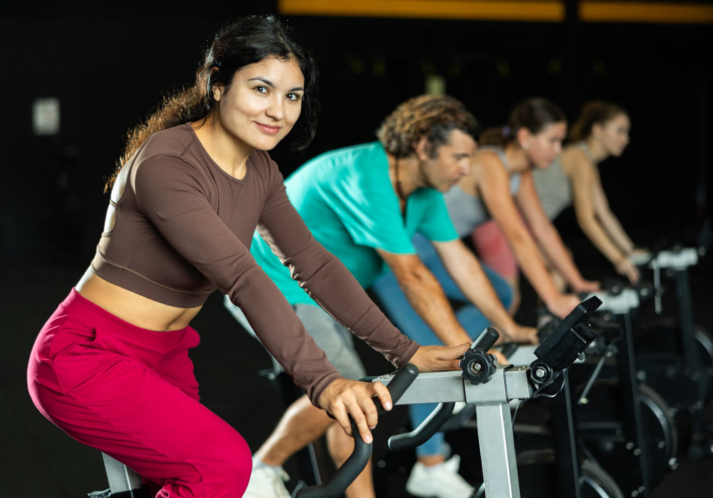 Positive Latina girl doing spin bike exercises in well-equipped gym