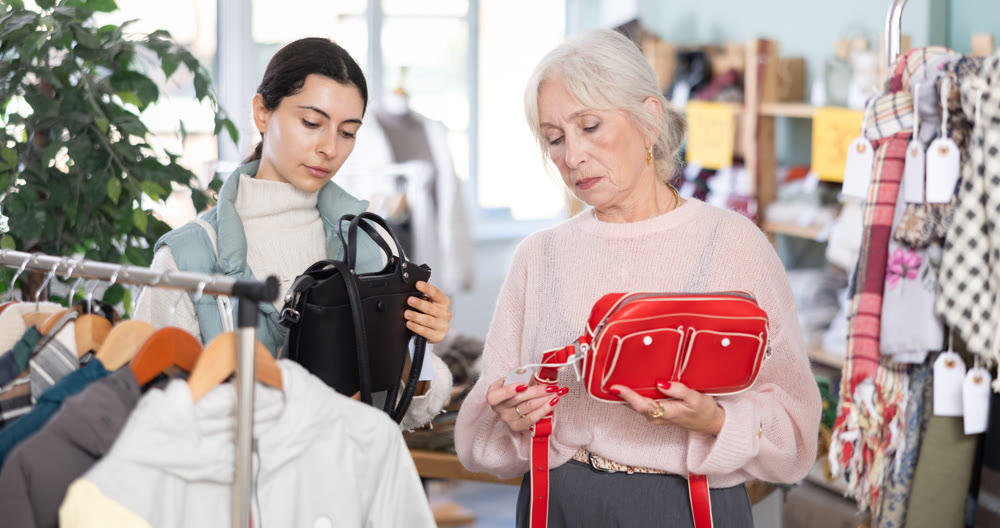 Elderly mother and her adult daughter choose together fashionable handbags in clothing store