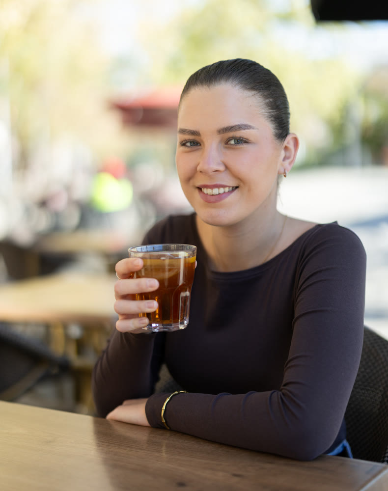 Woman drinking iced tea while sitting at table on cafe terrace