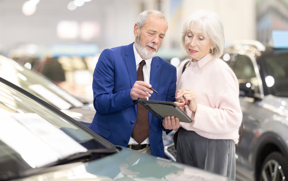 Elderly man seller showing tablet to woman in dealership