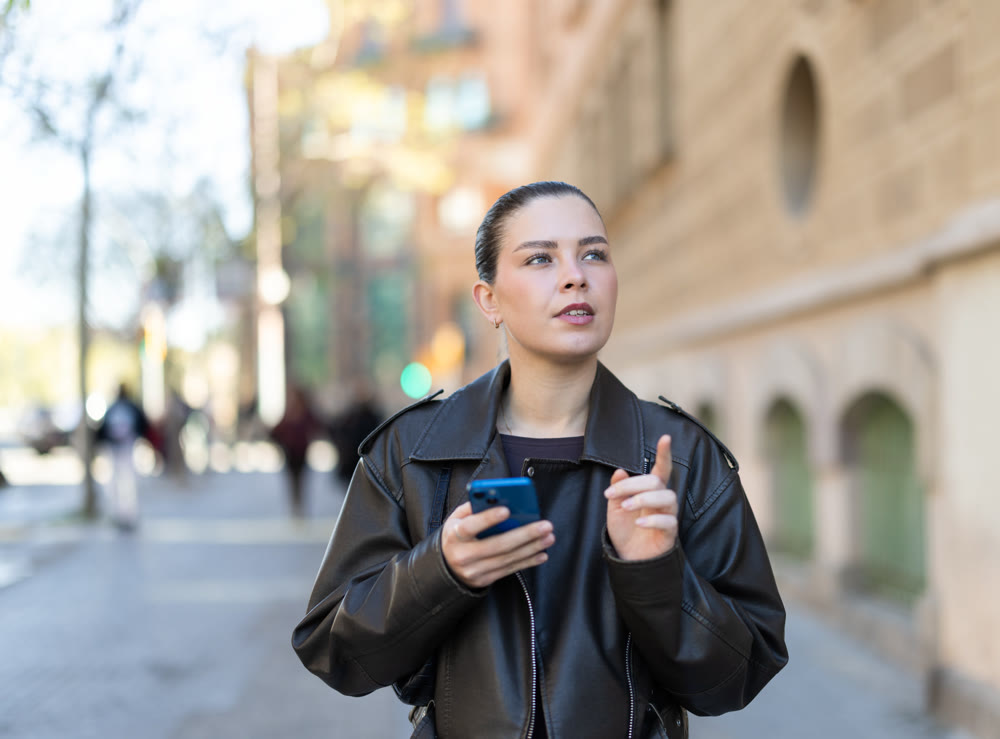 Joyful woman with a phone in hands walks around city, she looks at maps in mobile application