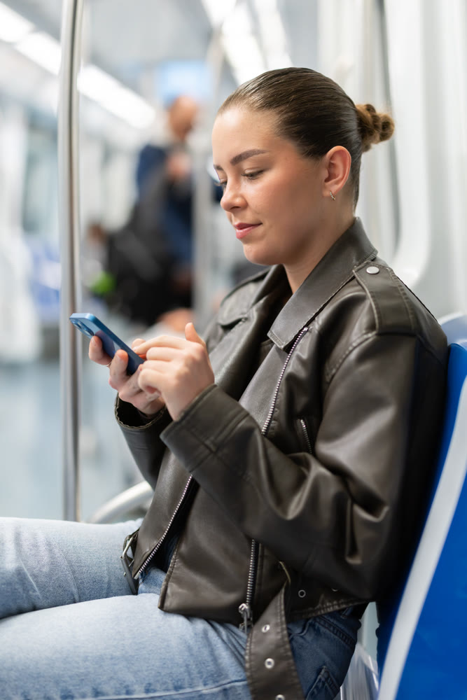 Young woman sitting in subway car with phone