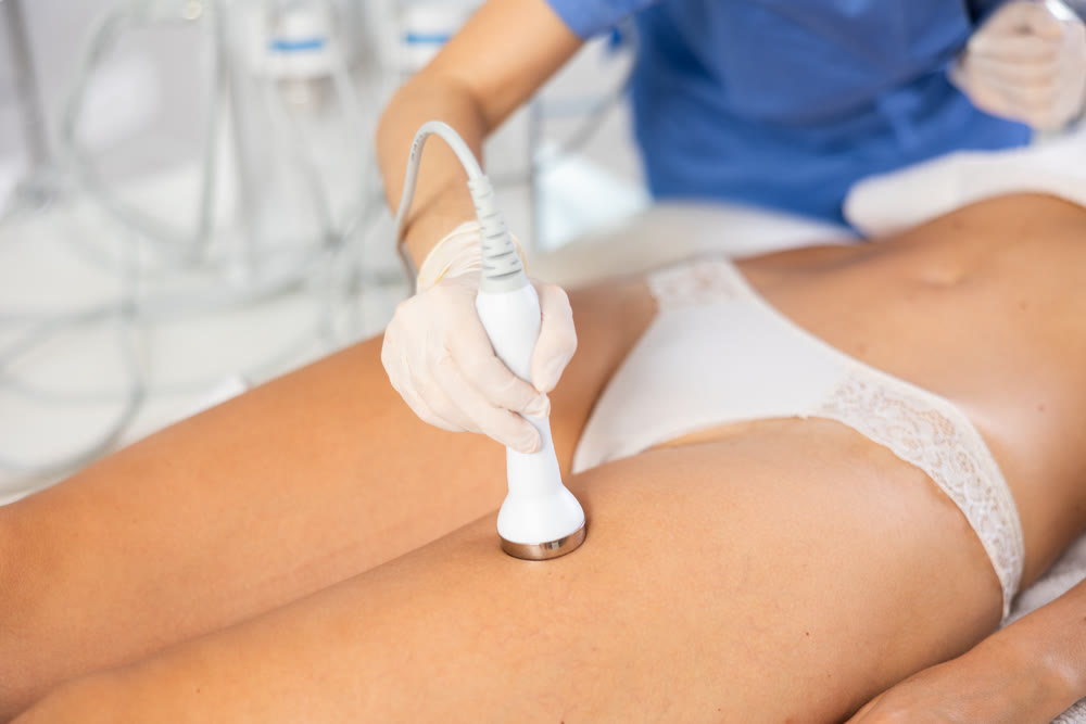 Young female cosmetologist performs ultrasound massage on thighs of young woman