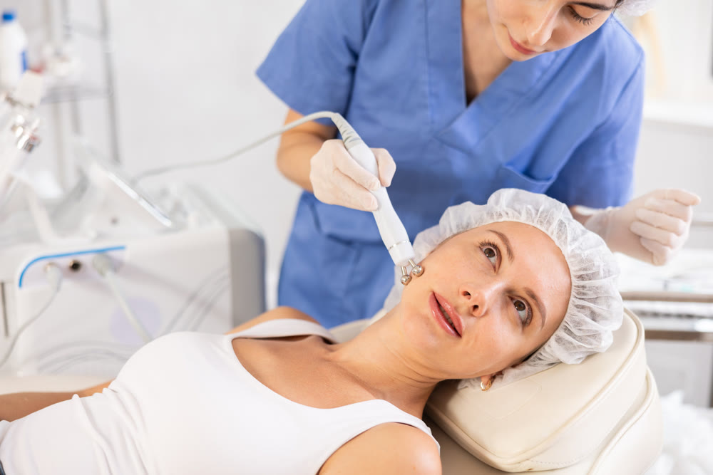 Young woman cosmetologist doing microcurrent procedure to young woman