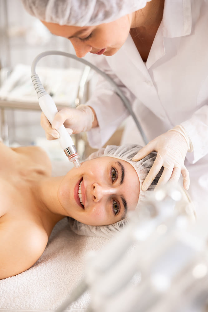 Young woman cosmetologist doing cleansing procedure to young woman