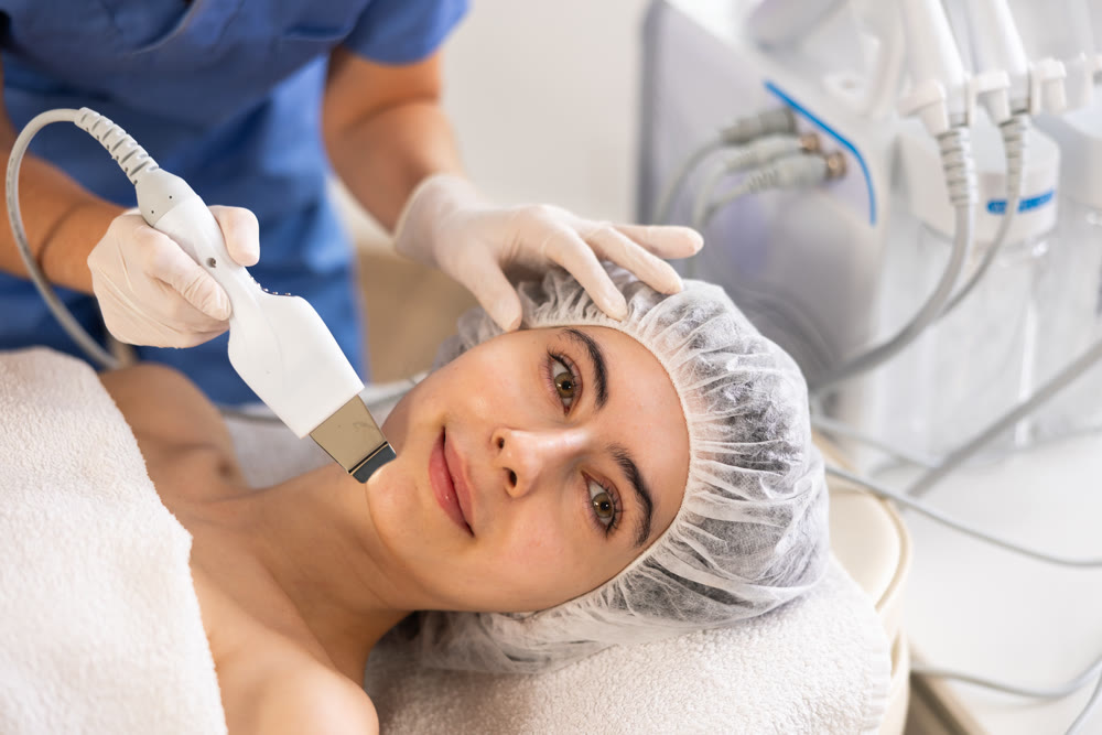 Young woman cosmetologist doing exfoliation procedure to young woman