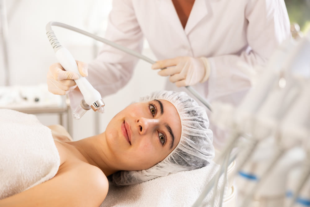 Young woman cosmetologist doing moisturizing procedure to young woman