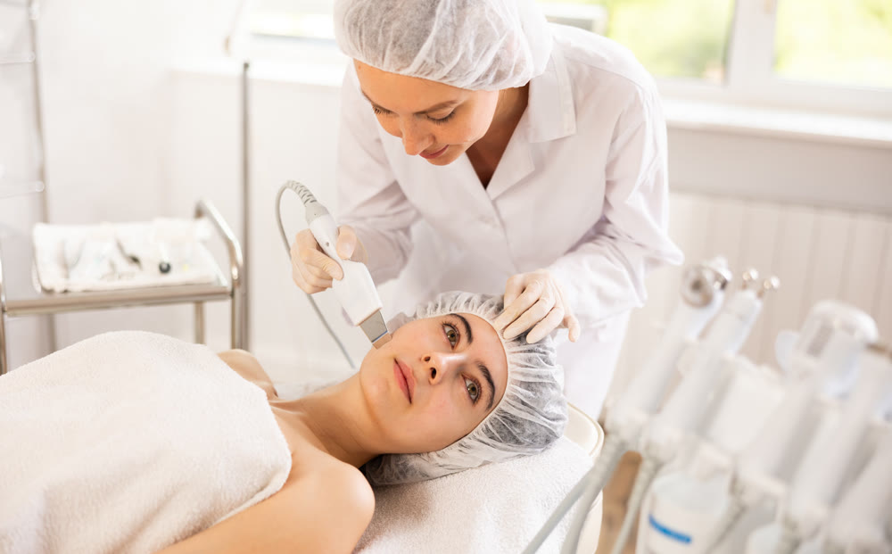 Young woman cosmetologist doing exfoliation procedure to young woman
