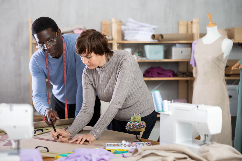 Woman tailor and African man companion draw dress pattern of product on paper