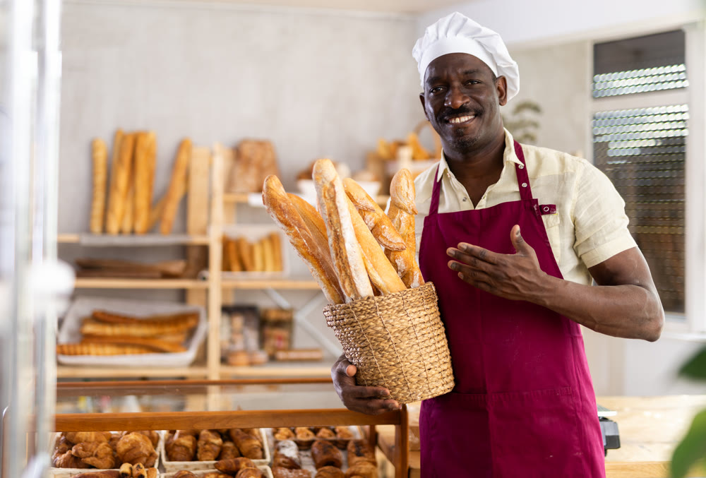 Portrait of male baker with bread and baguettes in hands in bakery
