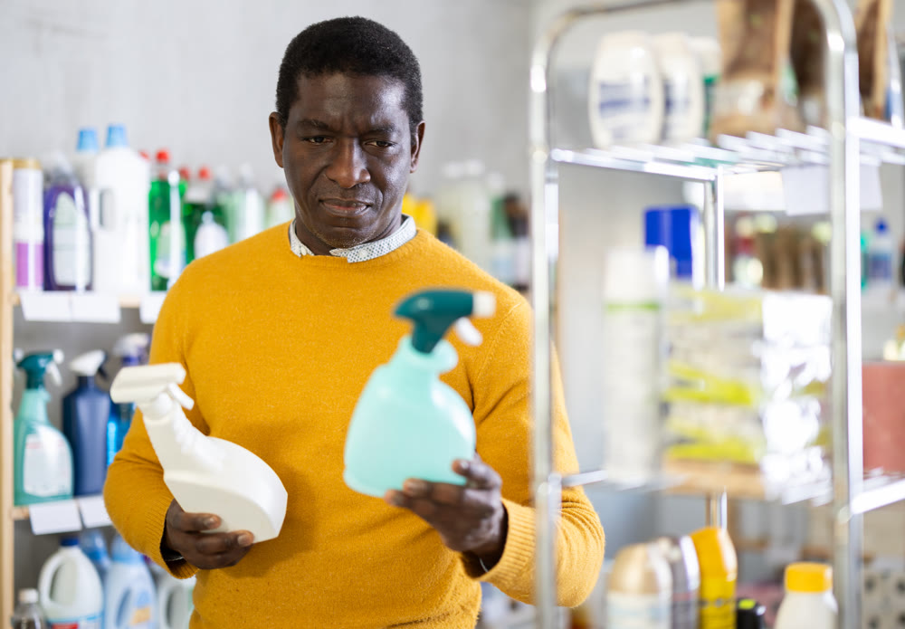 Before buying in household shop, African male customer choose glass cleaner spray