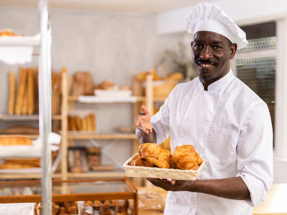 African male baker worker sells croissants, shows many products