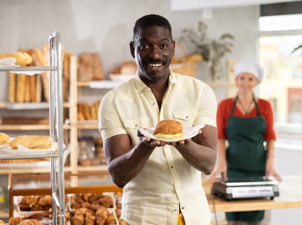 African man customer holding disposable plate with burger in bakery