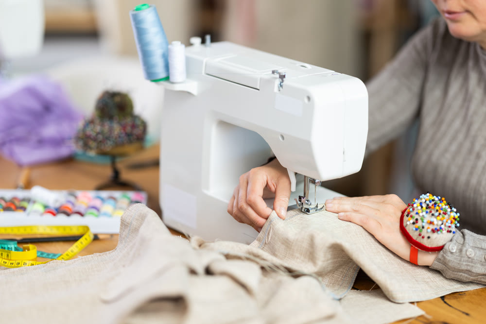 Hands of seamstress sewing checkered fabric on machine