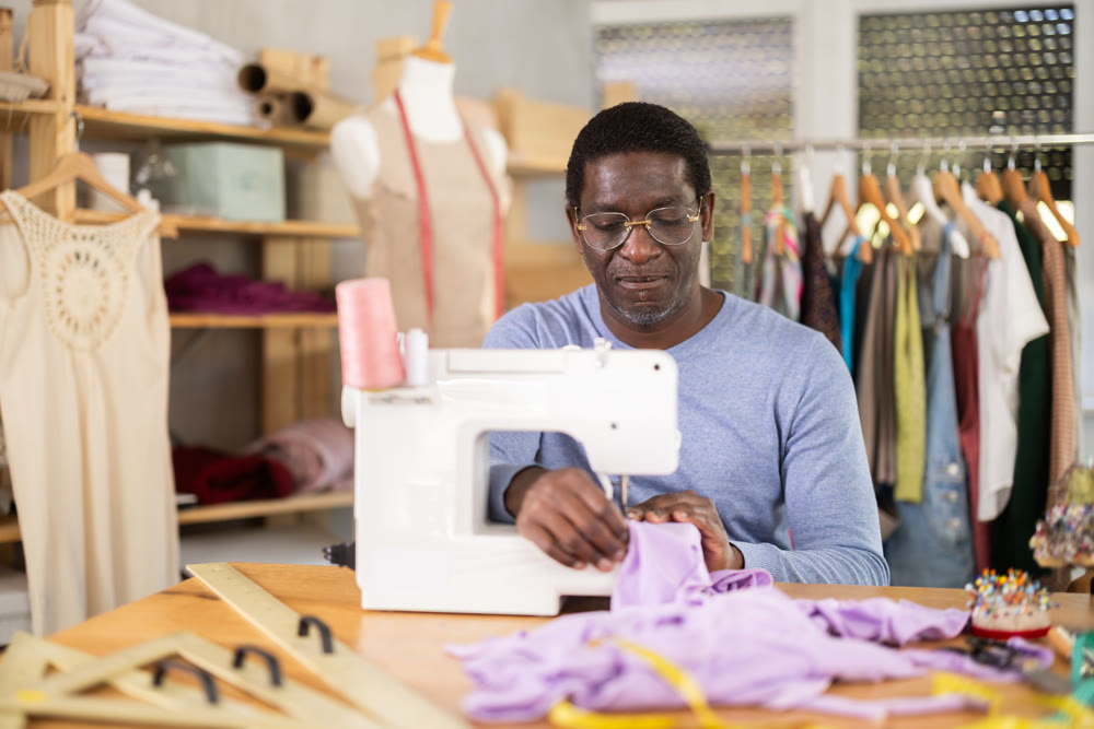 African American man tailor sews clothes in sewing machine.