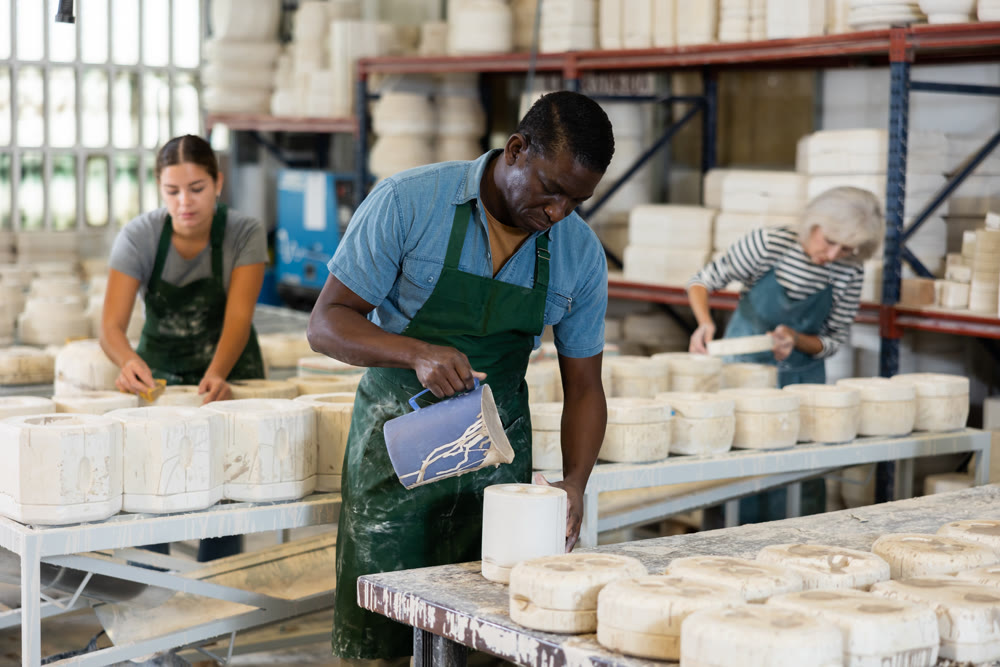 Slip casting - african american worker pours slip mass from jug into plaster mold in pottery factory