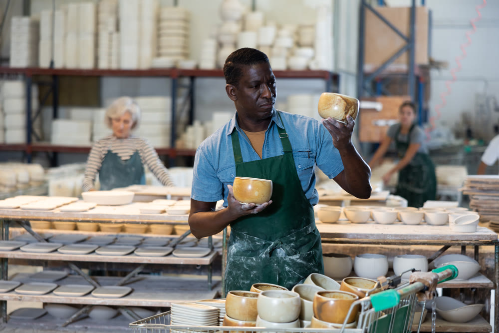African american man checks quality of pottery after being removed from plaster mold