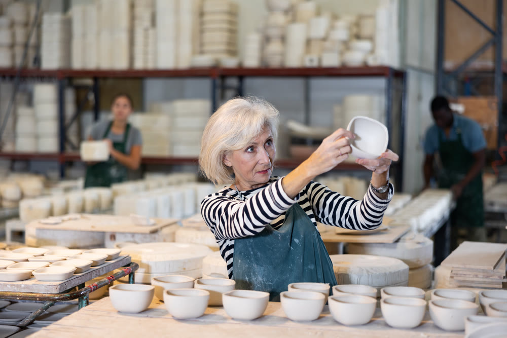 Portrait of positive senior woman holding ceramic cups at workshop