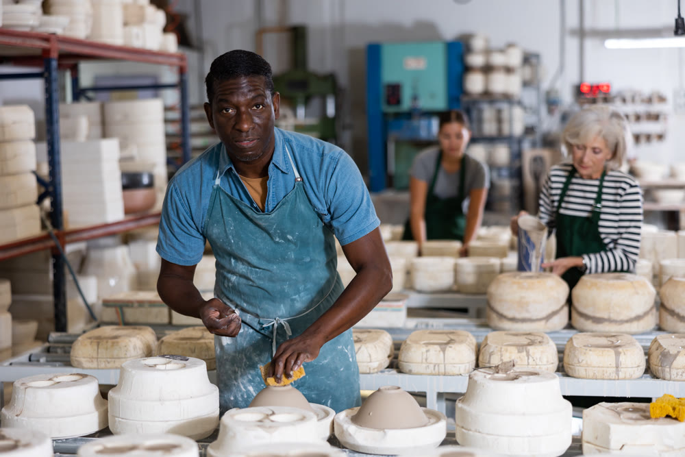 African american man prepares pottery with foam sponge - removes roughness and unevenness