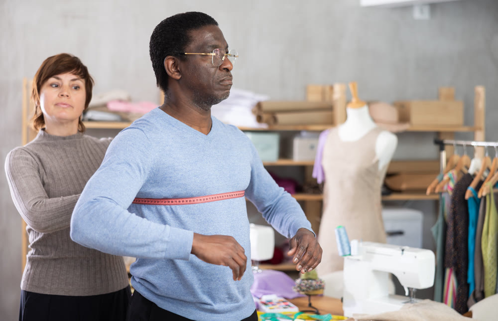 Female tailor using measuring tape to measure clothes on man in sewing studio