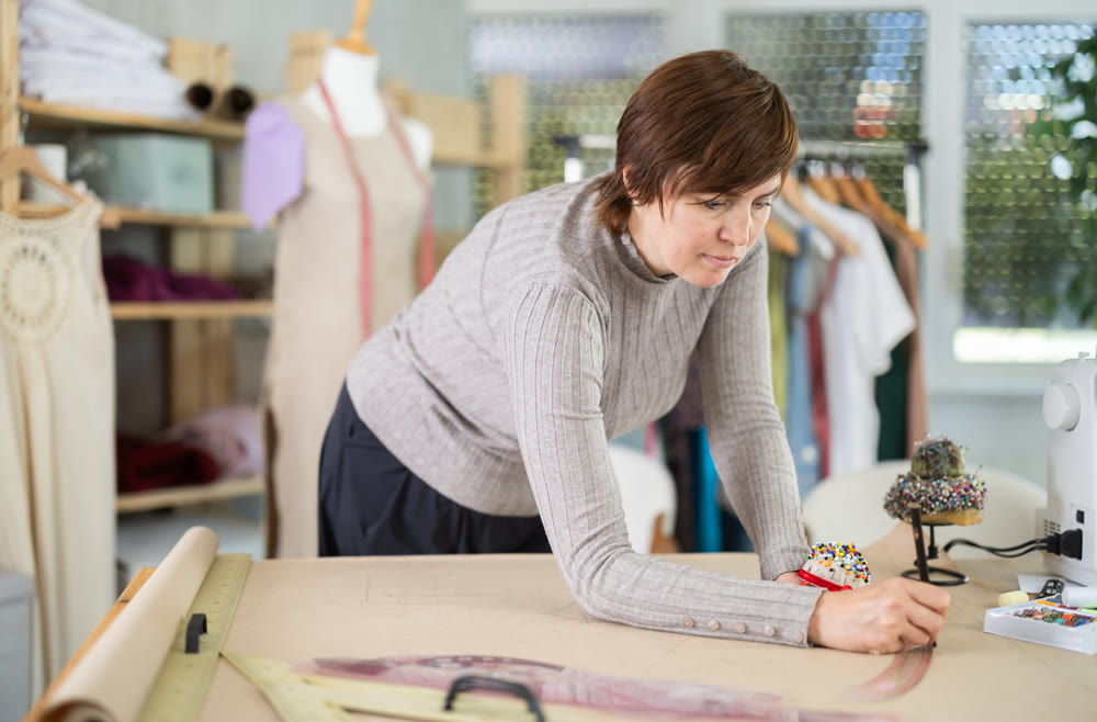 Female dressmaker draws sketch of future clothing on paper using patterns in sewing workshop