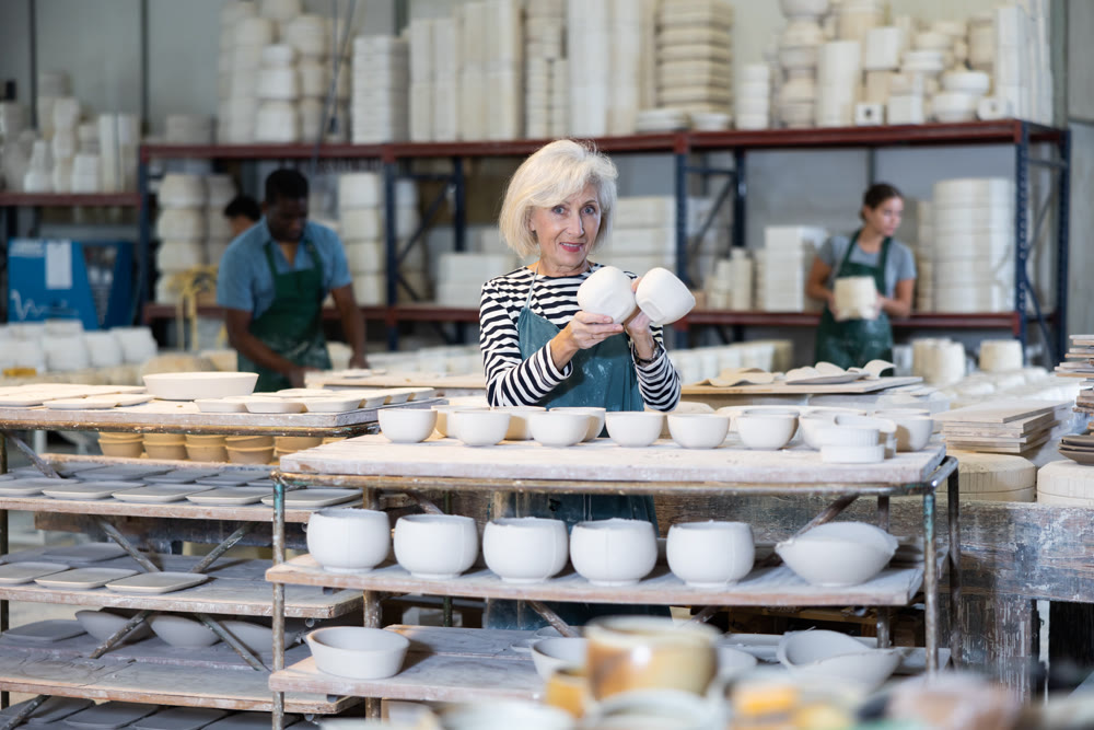 Portrait of craftswoman in a production workshop among ceramic cups and plates