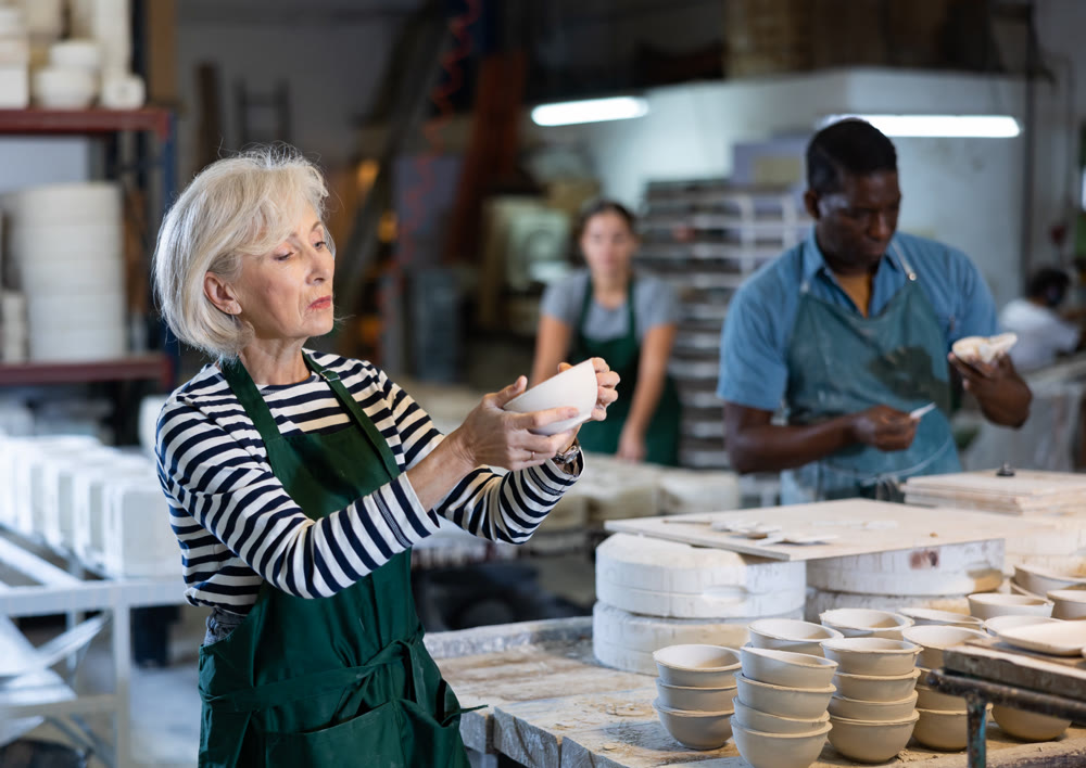 Mature craftswoman checking quality of pottery in pottery factory