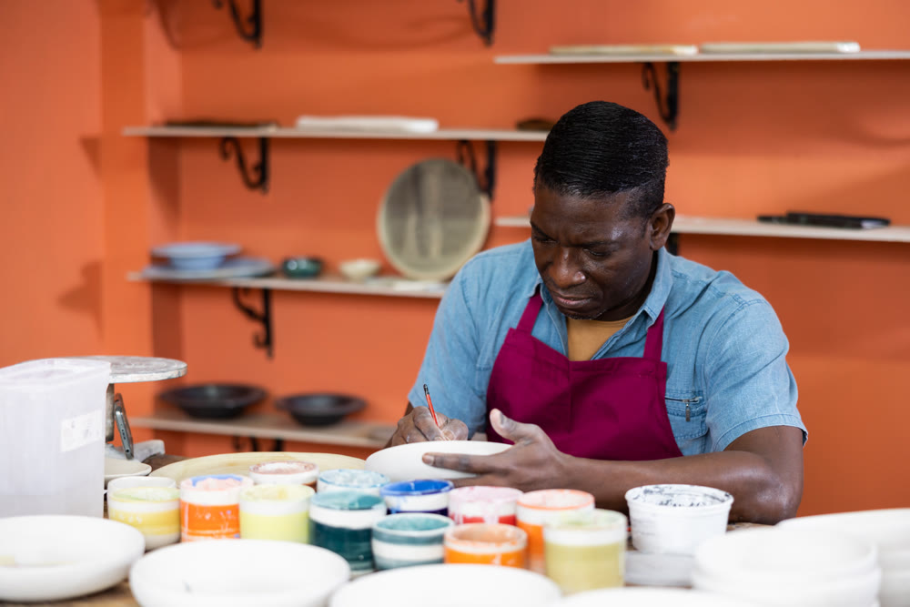 Male craftsman painting clay plates acrylic paints in art studio