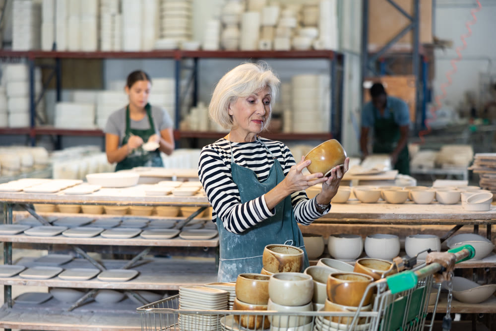 Portrait of craftswoman in a production workshop among ceramic cups and plates