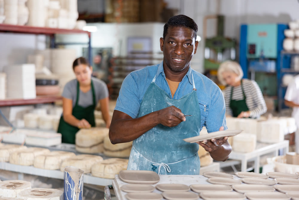 Positive man potter with new crafted crockry in workshop