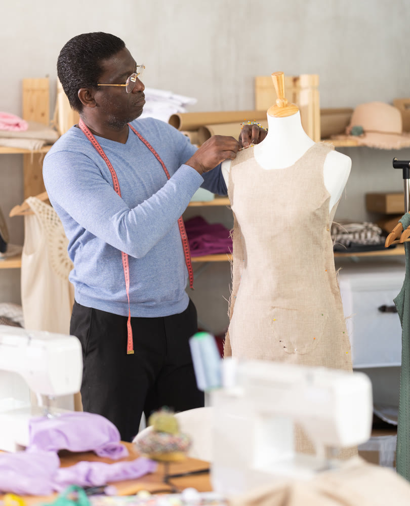 Male tailor sews new dress on a mannequin in sewing studio