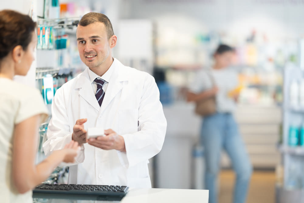 Male pharmacist speaking to woman customer buying medical preparation in drugstore