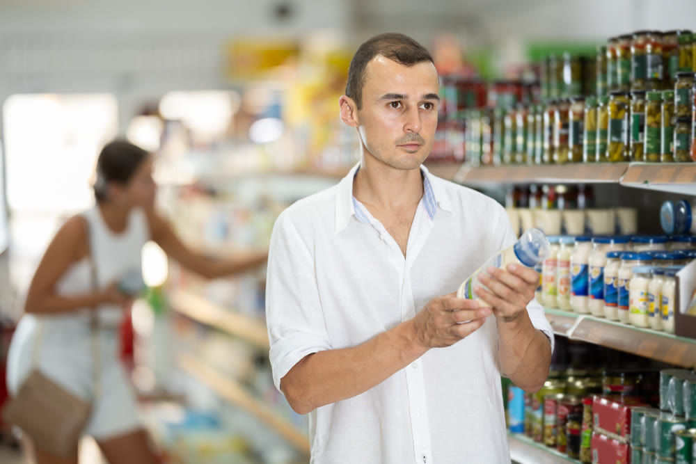 Male buyer chooses mayonnaise sauce in supermarket