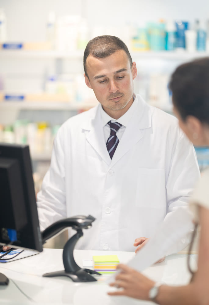 Male pharmacist at the cash register selling medicine to pharmacy visitor