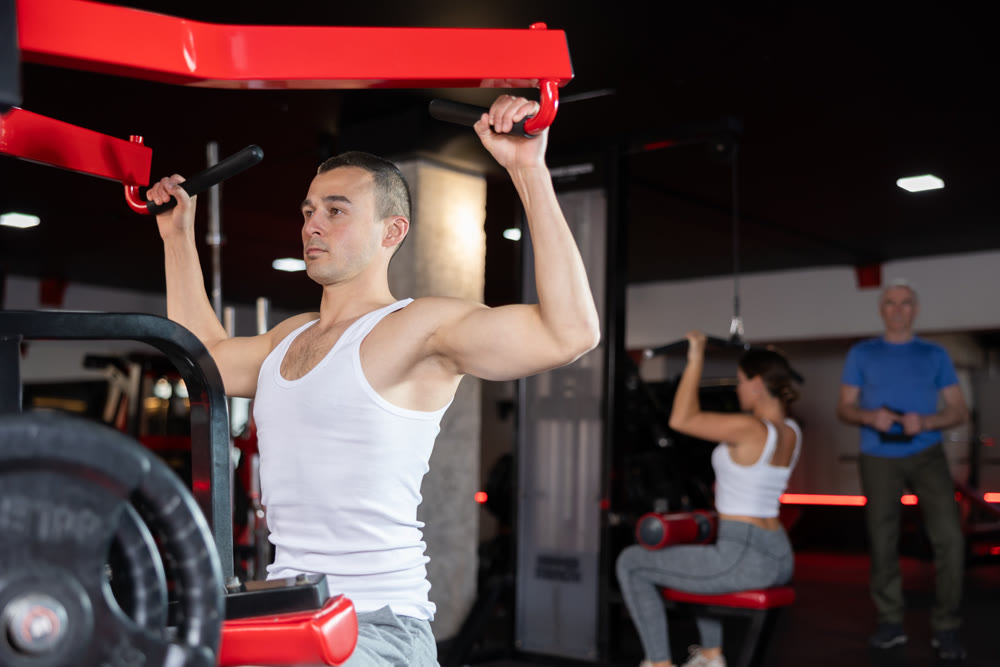 Portrait of man doing triceps curls in exercise machine during strength training in gym