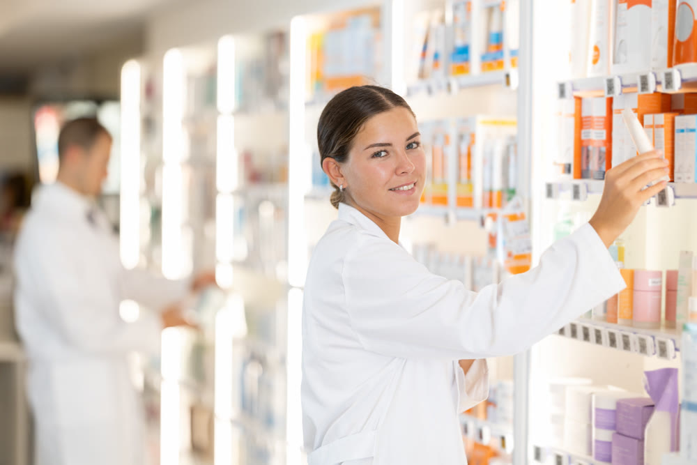 In chemist shop, woman consultant designs showcase with beauty care cosmetics