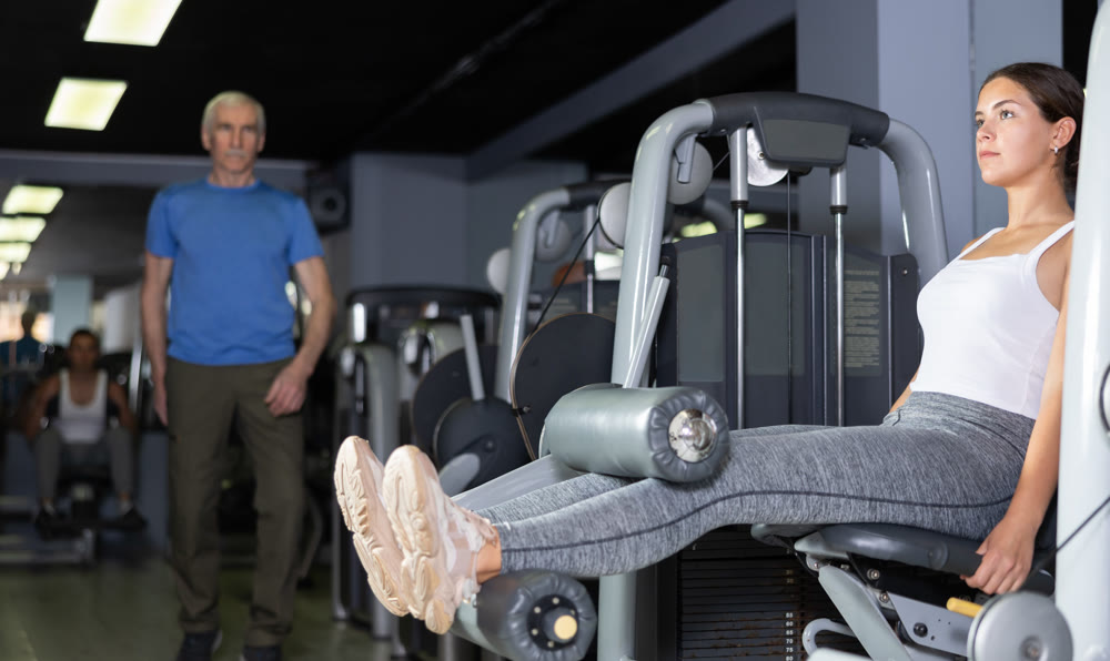 Girl in sportswear trains his leg muscles on machine in the gym
