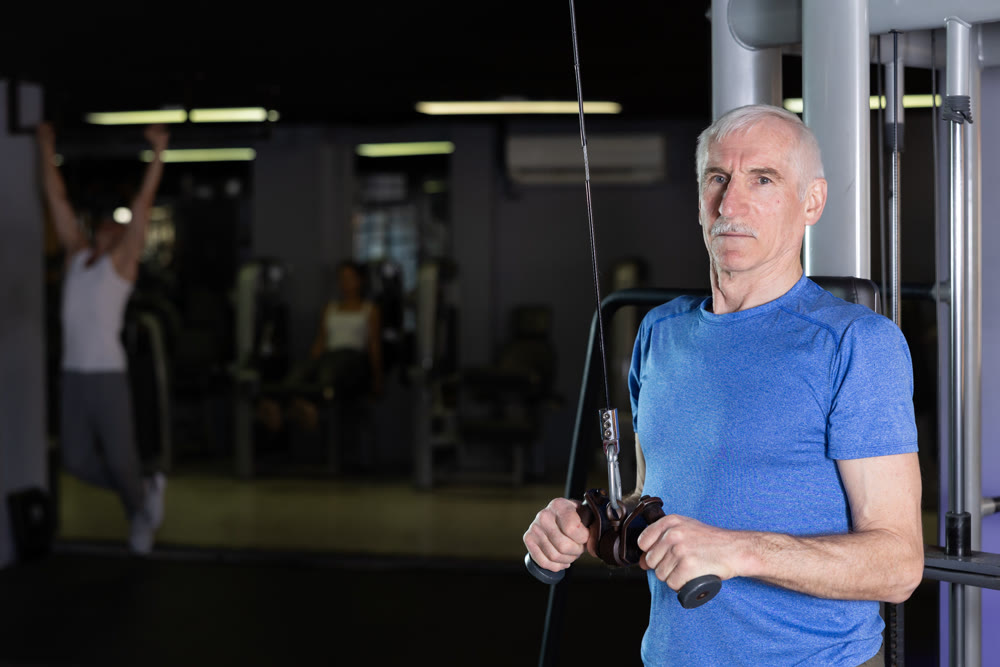 Mature man in sportswear training on rope loop simulator in gym