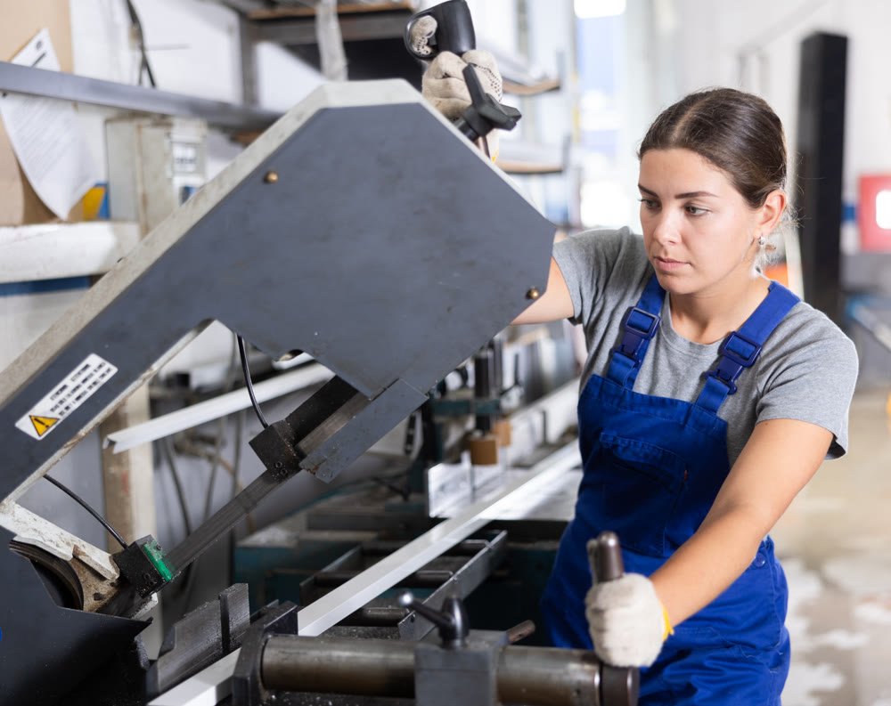 Female technician operating profile cutting machine in production workshop