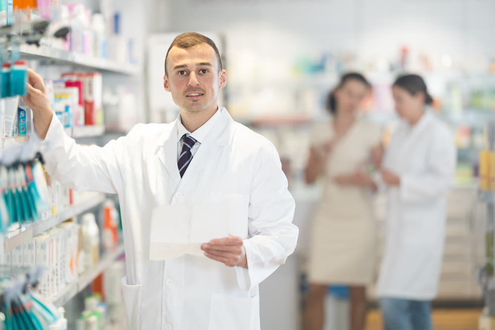 Positive male pharmacist in medical uniform posing while working in pharmacy
