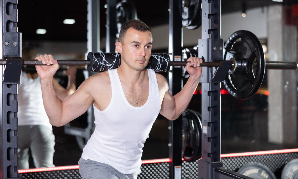 Sporty man performing set of exercises with barbell during intense workout