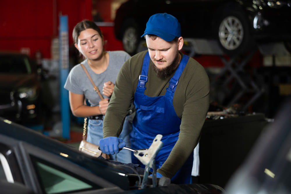 Young guy mechanic fixing woman client's car