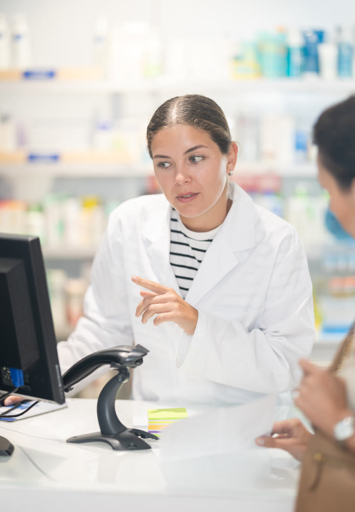 Female pharmacist at the cash register selling medicine to pharmacy visitor
